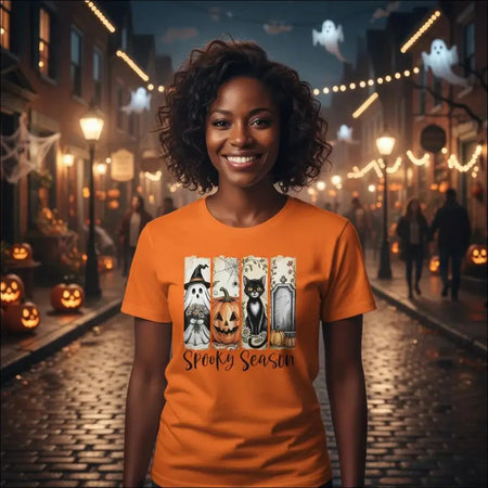 Orange short-sleeved Halloween t-shirt with spooky ghosts, pumpkins, cats, tombstones and Spooky Season text in Autumn Spooks Cotton Tee design